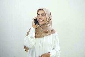 mooi glimlachen Aziatisch moslim vrouw vervelend hijab gebruik makend van mobiel telefoon, typen sms bericht geïsoleerd Aan wit achtergrond studio portret. mensen religieus levensstijl concept foto