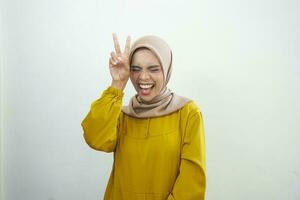 vrolijk moslim meisje in hijab tonen vrede gebaar en poseren naar camera studio achtergrond met vrij ruimte foto