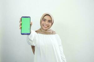 opgewonden mooi Aziatisch moslim vrouw tonen groen scherm mobiel telefoon geïsoleerd over- wit achtergrond foto