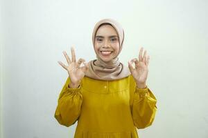glimlachen jong Aziatisch vrouw in wit gewoontjes tonen Oke gebaar geïsoleerd Aan wit achtergrond foto