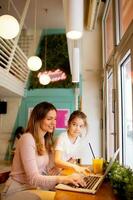 jong moeder en haar dochter werken Aan laptop en drinken vers oranje sap in de cafe foto