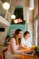 jong moeder en haar dochter werken Aan laptop en drinken vers oranje sap in de cafe foto
