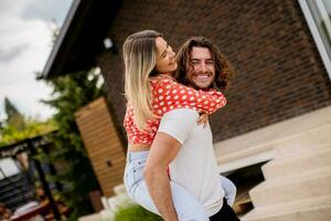 knap lang haar- Mens draag- de jong vrouw Aan zijn terug in voorkant van steen huis foto