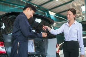 een jong Kaukasisch vrouw legt uit over haar auto problemen naar monteur Mens in auto reparatie winkel foto