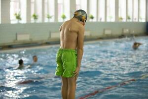 een jongen in een zwemmen pet en stofbril duiken in een sport- zwembad. foto