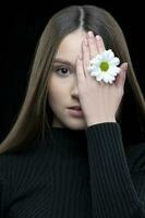 een mooi meisje met natuurlijk schoonheid houdt een wit bloem in de buurt haar oog. jong meisje met een wit chrysant. foto