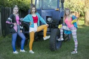 drie land meisjes gekleed in de stijl van de 90s staan door de tractor. foto