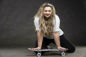 mooi dik vrouw met een skateboard Aan een grijs achtergrond looks Bij de camera en glimlacht. foto