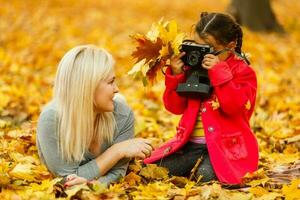 jong moeder spelen met haar dochter in herfst park foto