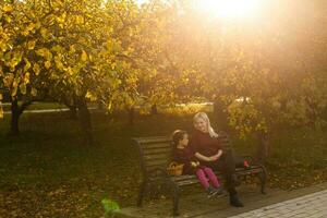 gelukkig moeder en dochter omarmen Aan een bank in een herfst park foto