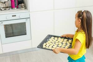 weinig meisje maakt koekjes van de deeg in de keuken Bij huis foto