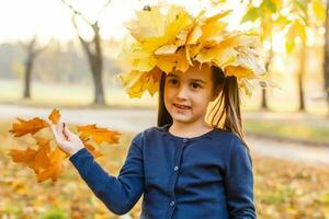 herfst seizoen vrije tijd. atmosfeer van herfst. aanbiddelijk glimlachen schoolmeisje herfst gebladerte achtergrond. mooi zo humeur. gelukkig kind. Welkom oktober. Verenigde met natuur. weinig kind wandelen in herfst park. foto