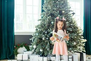 weinig meisje op zoek fotoboek in voorkant van Kerstmis boom foto