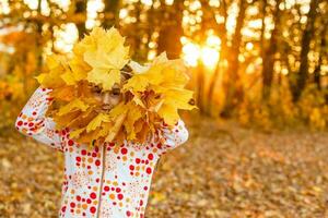 herfst seizoen vrije tijd. atmosfeer van herfst. aanbiddelijk glimlachen schoolmeisje herfst gebladerte achtergrond. mooi zo humeur. gelukkig kind. Welkom oktober. Verenigde met natuur. weinig kind wandelen in herfst park. foto