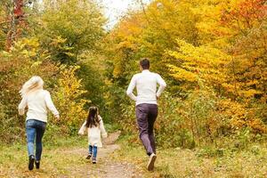 afbeelding van lief familie in herfst park, jong ouders met mooi hoor aanbiddelijk dochter spelen buitenshuis, hebben pret Aan achtertuin in val, gelukkig familie genieten herfst- natuur foto
