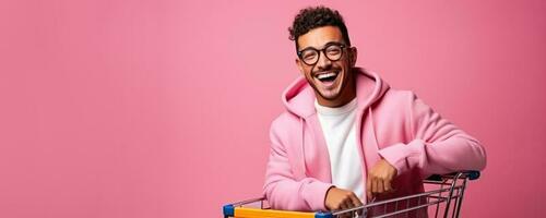 portret van een jong latino Mens in bril met een boodschappen doen kar Aan een roze achtergrond met leeg ruimte voor tekst foto