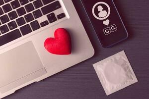rood hart Aan laptop met telefoon en condoom voor online dating liefde babbelen bij elkaar passen flirterig concept. foto