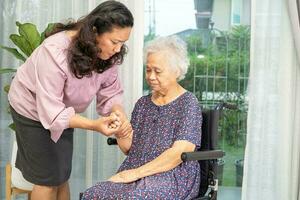 verzorger helpen Aziatisch senior vrouw Aan rolstoel met liefde Bij huis. foto
