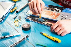 tovenaar repareert laptop met gereedschap en handen op de blauwe houten tafel. bovenaanzicht foto