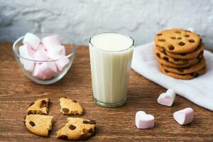 zelfgemaakte chip cookies met melk en lucht marshmallow op keukenhanddoek en houten tafel. Goedemorgen. ontbijt concept foto