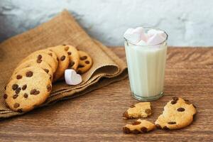 geurige, smakelijke, zelfgemaakte koekjes met rozijnen, marshmallow in hartvorm en een glas verse melk op tafel foto