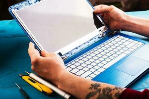 tovenaar repareert laptop met gereedschap en handen op de blauwe houten tafel. bovenaanzicht foto