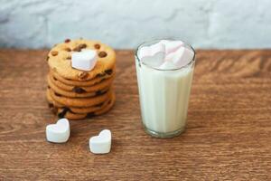 geurige, smakelijke, zelfgemaakte koekjes met rozijnen, marshmallow in hartvorm en een glas verse melk op tafel foto