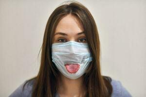 grappig meisje dat een chirurgisch masker draagt en haar tong laat zien. foto