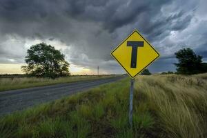 weg kruispunt waarschuwing teken met een stormachtig lucht achtergrond, la pampa provincie, Patagonië, Argentinië. foto
