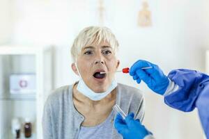 volwassen Kaukasisch vrouw in een klinisch instelling wezen uitstrijkje door een gezondheidszorg arbeider in beschermend gewaad naar bepalen als ze heeft gecontracteerd de coronavirus of covid19. foto