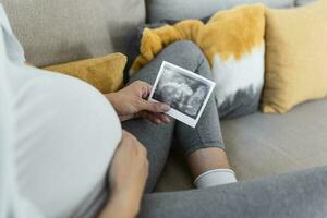 zwanger vrouw Holding echografie afbeelding. concept van zwangerschap, Gezondheid zorg, gynaecologie, geneesmiddel. jong moeder aan het wachten van de baby. detailopname, kopiëren ruimte, binnenshuis. foto