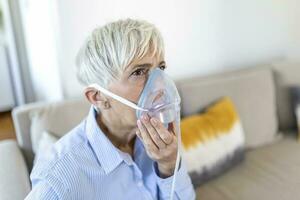 ziek ouderen vrouw Aan zuurstof masker inademing, longontsteking coronavirus pandemie. ziek senior vrouw vervelend een zuurstof masker en ondergaan behandeling. senior vrouw met covid 19 foto