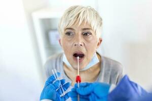 volwassen Kaukasisch vrouw in een klinisch instelling wezen uitstrijkje door een gezondheidszorg arbeider in beschermend gewaad naar bepalen als ze heeft gecontracteerd de coronavirus of covid19. foto