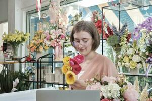 een jong wit Aziatisch vrouw bloemist ondernemer bloesems regelen van, decoreren, gelukkig werk in kleurrijk bloem winkel op te slaan met bloeit, en klein bedrijf baasje. foto