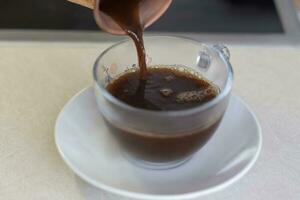 zwart vers gebrouwen koffie is gegoten van een koper kop in een beker. ontbijt met koffie. maken koffie in een Turk. foto