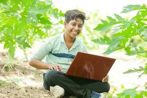 Indisch jongen aan het studeren in boerderij, Holding laptop in hand- , arm Indisch kinderen foto