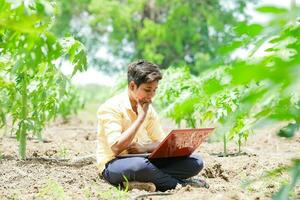 Indisch jongen aan het studeren in boerderij, Holding laptop in hand- , arm Indisch kinderen foto