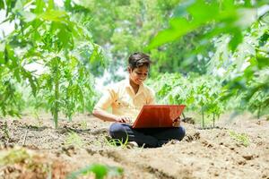 Indisch jongen aan het studeren in boerderij, Holding laptop in hand- , arm Indisch kinderen foto