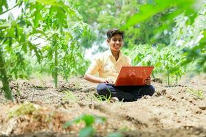 Indisch jongen aan het studeren in boerderij, Holding laptop in hand- , arm Indisch kinderen foto