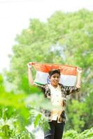 Indisch jongen Holding nationaal vlag in boerderij, gelukkig jongen, nationaal vlag foto