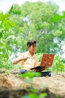 Indisch jongen aan het studeren in boerderij, Holding laptop in hand- , arm Indisch kinderen foto