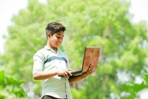 Indisch jongen aan het studeren in boerderij, Holding laptop in hand- , arm Indisch kinderen foto