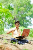 Indisch jongen aan het studeren in boerderij, Holding laptop in hand- , arm Indisch kinderen foto