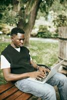 jong zwart Mens werken Aan laptop buitenshuis, op zoek Bij scherm, gefocust Aan werk foto