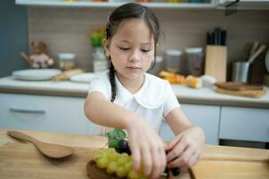 schattig weinig meisje in een wit keuken van gezond fruit en groenten, lachend. foto