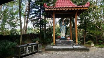 standbeeld van de maagd Maria onder een luifel met bomen in de achtergrond, in de jatiningsih Maria grot, jogjakarta, waar katholieken bidden, geven bedankt en verzenden verzoeken naar god foto