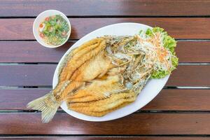 gebakken snapper vis blanco in wit bord Aan hout tafel geserveerd met vis saus en groenten. foto