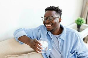 jong Afrikaanse Mens in vrijetijdskleding drinken water van glas foto