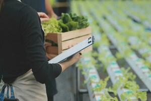 Aziatisch vrouw boer gebruik makend van digitaal tablet in groente tuin Bij serre, bedrijf landbouw technologie concept, kwaliteit slim boer. foto