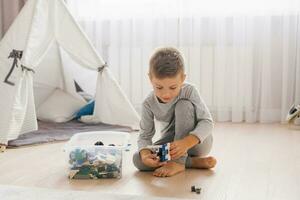 jongen kind Toneelstukken met speelgoed, verzamelt een bouwer in een knus kinderen kamer foto